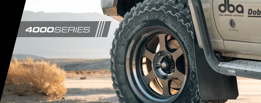 Close-up of 4WD vehicle wheel on desert terrain with DBA 4000 Series branding prominently displayed on vehicle body, showcasing off-road brake performance