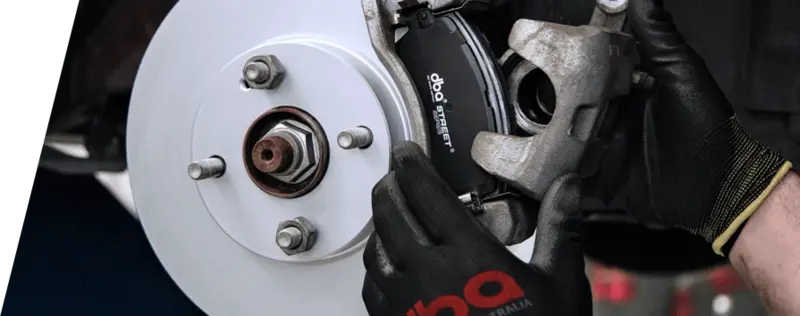 Mechanic in DBA-branded gloves installing brake rotor and caliper on vehicle wheel hub