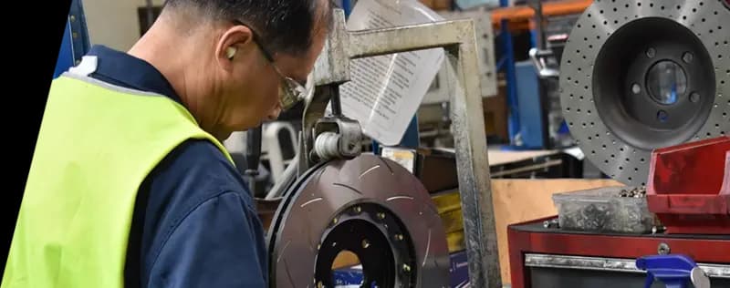 DBA factory technician in safety gear working on brake rotor production with specialized equipment in manufacturing facility