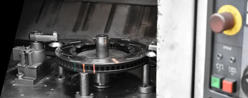 DBA brake rotor with colored temperature indicators being manufactured on precision CNC machine with control panel visible in background