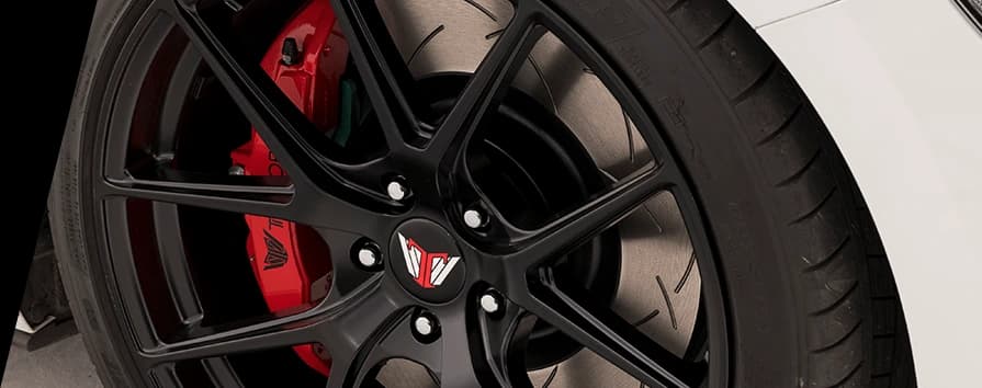 Performance brake setup featuring slotted DBA brake rotor with red caliper visible through black wheel spokes