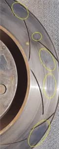 Brake rotor with visible friction material deposits that can lead to steering wheel vibration and uneven braking performance Close-up of brake rotor surface showing irregular friction material deposits highlighted with yellow circles causing brake shudder