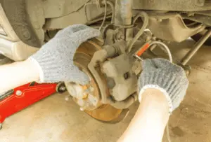 Proper technique for opening brake caliper bleeder valve with wrench and collection tube during brake system bleeding procedure Mechanic's gloved hands opening brake caliper bleeder valve with wrench while clear tube is attached to capture fluid during brake bleeding