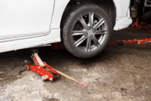 Hydraulic floor jack and safety stands setup for safely elevating vehicle during brake system bleeding procedure Hydraulic floor jack positioned under vehicle with safety jack stands visible for proper support during brake bleeding maintenance