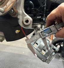 Step 2D: Measuring bottom clearance cut distance of approximately 41mm from backing plate edge for precise modification Digital caliper measuring approximately 41mm from edge of backing plate for bottom clearance cut during DBA brake upgrade installation