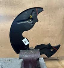 Step 3A: Backing plate removed from vehicle and secured in vice for cutting along marked lines for DBA caliper clearance Removed backing plate positioned in vice showing cut lines marked with paint pen ready for modification during DBA brake upgrade installation