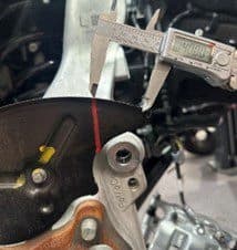 Step 2C: Measuring top clearance cut distance of approximately 40mm from backing plate edge for precise modification Digital caliper measuring approximately 40mm from edge of backing plate for top clearance cut during DBA brake upgrade installation
