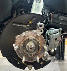 Step 1B: Original equipment backing plate exposed after caliper removal in preparation for DBA brake rotor installation Close-up of vehicle wheel hub with caliper removed showing backing plate and exposed hub assembly during DBA brake upgrade installation