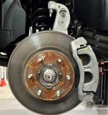 Step 1A: Original equipment brake assembly showing rotor and caliper that will be replaced during DBA brake upgrade procedure Close-up of original equipment (OE) brake assembly showing rusted rotor surface, caliper and mounting bracket before DBA brake upgrade installation